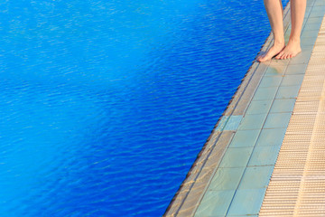 Young woman legs standing on border front of swimming pool 