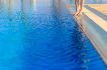 Young woman legs standing on border front of swimming pool 