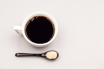 White coffee cup with coffee and black teaspoon with brown sugar