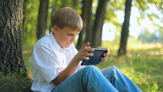 Caucasian child teen boy teenager playing uses touchscreen gadget Tablet PC