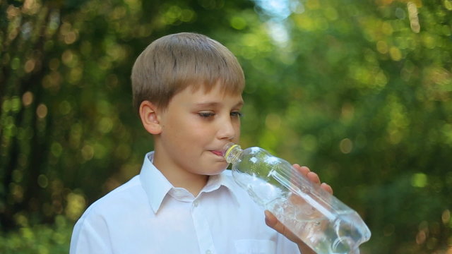 Caucasian child teen boy drinks water from a plastic bottle. Summer hot weather