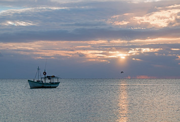 Fishing boat in Puerto Juarez at sunrise with pelican flying by through sunray