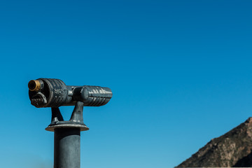Sightseeing Binoculars with background of sky and portion of mountain.