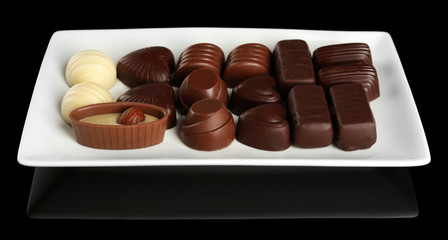Assorted chocolate candies on white plate over black background