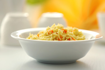 Stewed rice with a carrot in a white bowl on a table, close up