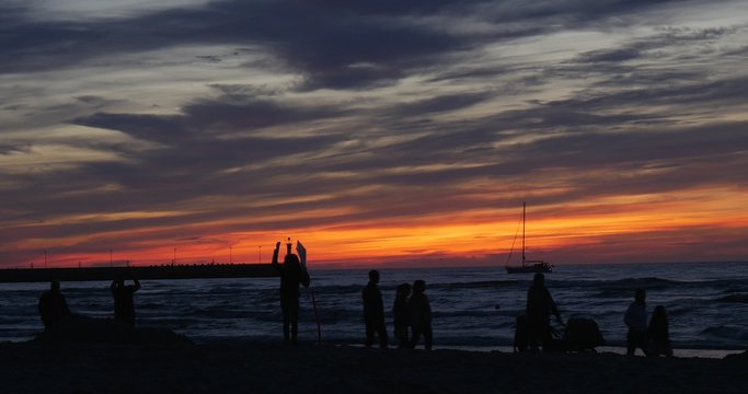 People Families Silhouettes Point to Something People Are Walking by Sandy Beach Yacht on a Horizon Bright Pink and Yellow Sunset Waves on the Sea Pier