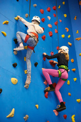 Two athlete girls climbing on blue wall