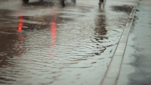 Rain. Cyclists and cars go through the puddles . Rain on the street, bad weather. Puddles on the road and the sidewalk, rain drops fall on the ground