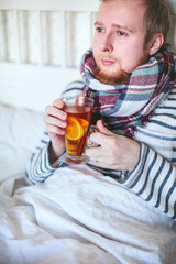 sick man with a scarf drinking hot tea in bed