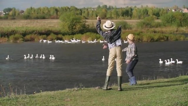 Rear view of two boys who look like Tom Sawyer and Huckleberry Finn throwing stones into the lake 