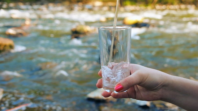 glass of pure mineral water on the background of a mountain stream. Female, miss, lady