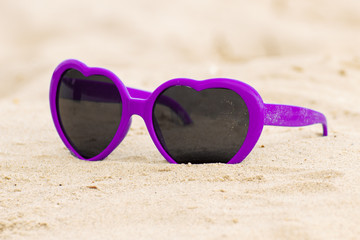 Fototapeta na wymiar Purple sunglasses shaped heart on the sand