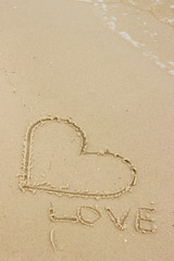 Word love and heart written on sand at the beach by the sea