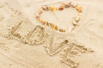 Word love written on sand at the beach, heart of shells