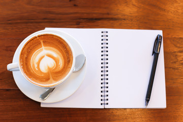 Coffee cup and notebook on table background.