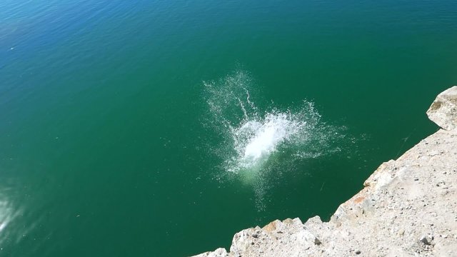 Teen boy jumping off a cliff rock into the water, extreme