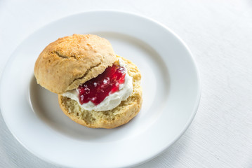 Scone with cream and cherry jam on the plate