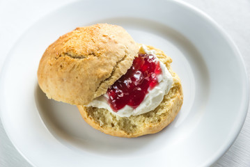 Scone with cream and cherry jam on the plate