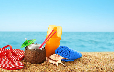 Flip-flops, sunscreen spray and coconut cocktail on the beach.