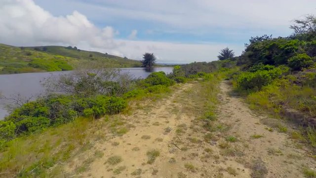 Aerial view of camera tracking at low altitude over a trail next to a Northern California serine pond camera fly&rsquo;s over trail bushes then pond booms up to reveal farmland and Pacific Ocean 