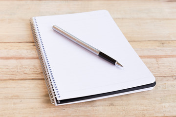 Blank white notebook with pen on wood desk. shallow depth of field