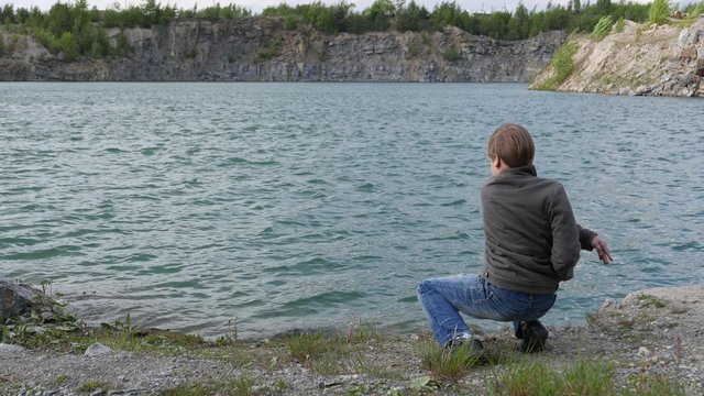 teen boy throwing stones into the water of the lake. Childhood dreams and memories. Ecology and environment, fresh air, clean water