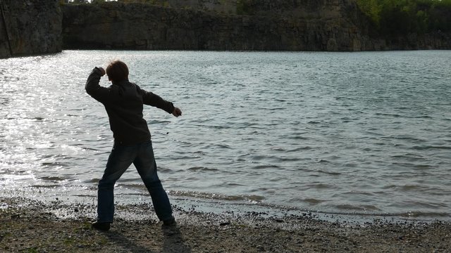 teen boy throwing stones into the water of the lake. Childhood dreams and memories. Ecology and environment, fresh air, clean water