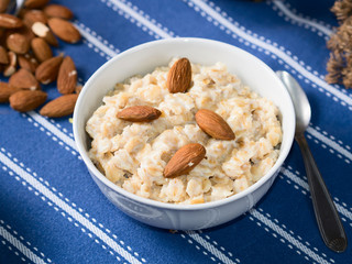 Oatmeal porridge with pears, honey and almonds for breakfast on dark blue table cloth
