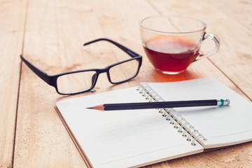 tea in glass and notebook,pencil with glasses on wood