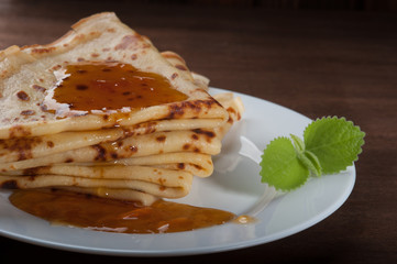 A stack of pancakes with jam on a white plate on dark wooden background 
