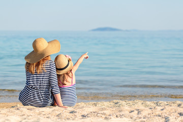Mother and daughter sitting next to each other at the beach while daughter is pointing with her hand