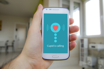 Hand holding smartphone with Cupid calling on the screen for Valentines day