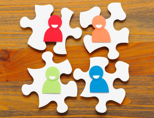 Four paper people discussing. Concept image of meeting and teamwork.Four puzzle pieces and paper people. Wooden background.


