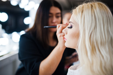 Young beautiful blonde bride applying wedding make up by makeup