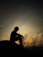 silhouette of boy sitting on rock at sunrise