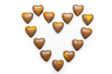 Milk heart shaped chocolates with yellow embellishment arranged in heart on white background directly from above