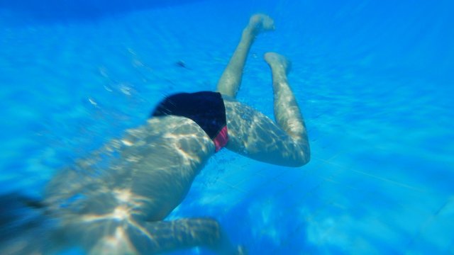 Caucasian child boy teen dives underwater in outdoor swimming pool. Sun tanning, swimming, tourism, rest and relaxation .