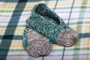 knitting warm winter slippers on plaid background