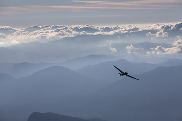 Fototapeta na wymiar Sillhouette of small plane over clouds and mountains