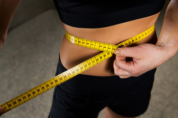 close up of woman measuring waist by tape in gym