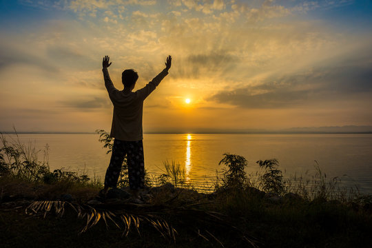 Silhouette of Asian man is refreshing by raising arms on riverside to the sunrise or sunset. Scenery of Pa Sak Chonlasit reservoir, Lopburi province, Thailand.