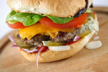 Tasty cheese beef burger with lettuce, cheddar, barbecue sauce, tomatoes, pickles and tzatziki