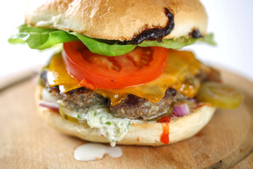 Tasty cheese beef burger with lettuce, cheddar, barbecue sauce, tomatoes, pickles and tzatziki