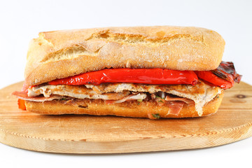 Tasty pork grilled serranito sandwich in a ciabatta with ham and red pepper on a white background