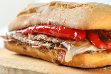 Tasty pork grilled serranito sandwich in a ciabatta with ham and red pepper on a white background