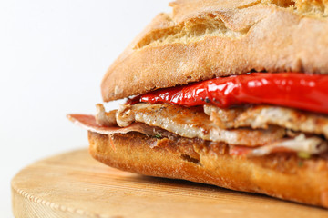 Tasty pork grilled serranito sandwich in a ciabatta with ham and red pepper on a white background