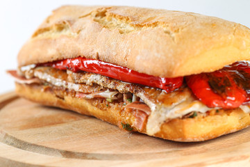 Tasty pork grilled serranito sandwich in a ciabatta with ham and red pepper on a white background