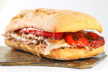 Tasty pork grilled serranito sandwich in a ciabatta with ham and red pepper on a white background