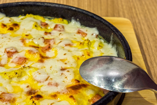 Baked omelet with cheese and opped with bacon in a wide black metal dish. The Korea menu is called Cheese Kyelanjim.