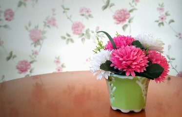 Pink and white artificial flowers in pot on wooden table